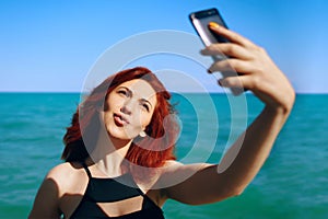 Red-haired woman takes selfie on smartphone camera.