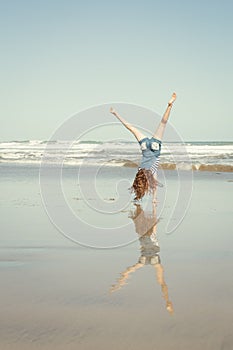 Red haired girl doing a hand stand or cartwheel on a New Zealand surf beach