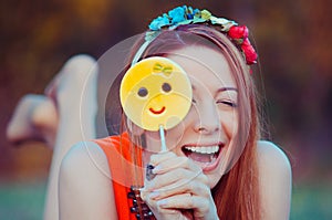 Red haired girl playing with yellow emoji candy on a stick