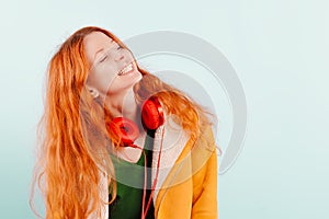 Red-haired girl in red headphones and yellow jacket laughs. Positive, happiness, joy and pleasure