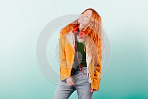 Red-haired girl in red headphones and yellow jacket laughs. Positive, happiness, joy and pleasure