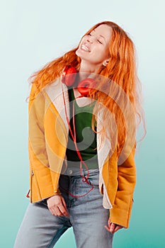 Red-haired girl in red headphones and yellow jacket laughs. Positive, happiness, joy and pleasure