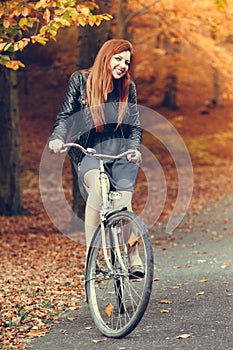 Red haired girl riding on bike in autumnal park