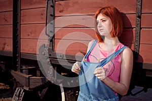 The red-haired girl with a short haircut is standing on an old, wooden train