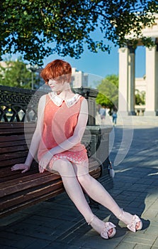 Red haired girl in a short pink dress on a park bench