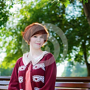 Red haired girl in a short pink dress on a park bench
