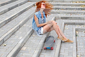 Red haired girl sitting near her scateboard and her hair fly by wind