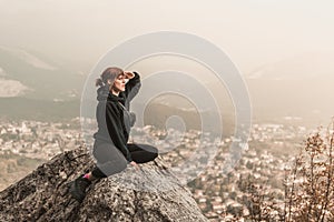 Red-haired girl is sitting on the stones above the precipice against the backdrop of mountains and fog