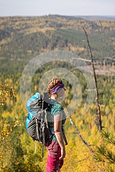 Red-haired girl standing with a backpack on a rock on a background of autumn forest