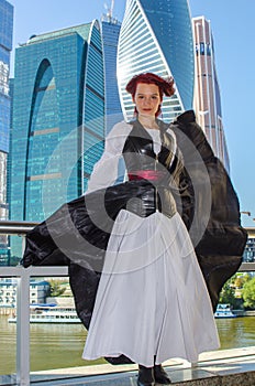 Red-haired girl stands on the bridge on the background of high-rise buildings