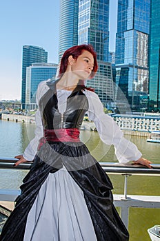 Red-haired girl stands on the bridge on the background of high-rise buildings