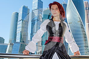 Red-haired girl stands on the bridge on the background of high-rise buildings