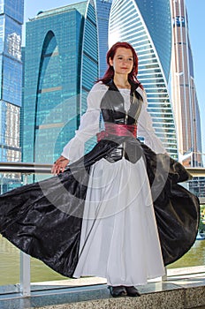 Red-haired girl stands on the bridge on the background of high-rise buildings