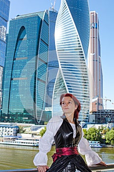 Red-haired girl stands on the bridge on the background of high-rise buildings