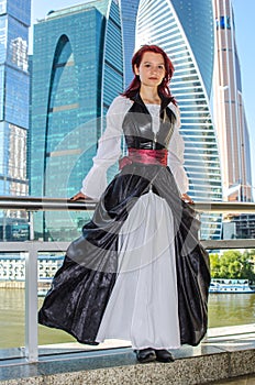 Red-haired girl stands on the bridge on the background of high-rise buildings