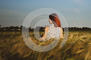 Red-haired girl stands in a field of grain turned back to photograph.