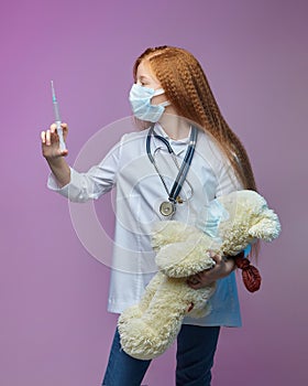 Red-haired girl and a Teddy bear in medical masks. the child is holding a syringe. the concept of prevention covid-19