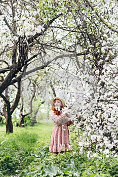 Red-haired girl walks in a spring blooming apple orchard