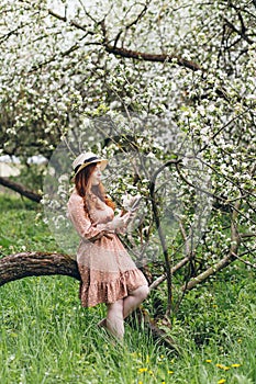 Red-haired girl walks in a spring blooming apple orchard