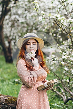 Red-haired girl walks in a spring blooming apple orchard