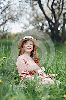 Red-haired girl walks in a spring blooming apple orchard