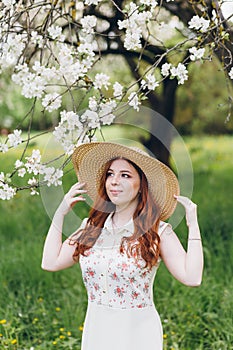 Red-haired girl walks in a spring blooming apple orchard