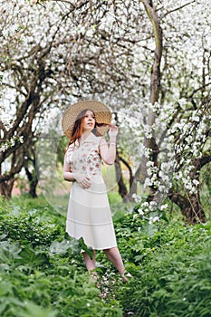 Red-haired girl walks in a spring blooming apple orchard