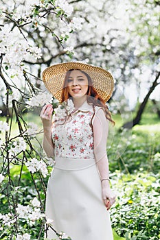 Red-haired girl walks in a spring blooming apple orchard