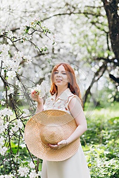 Red-haired girl walks in a spring blooming apple orchard