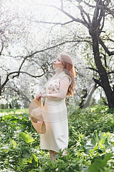 Red-haired girl walks in a spring blooming apple orchard