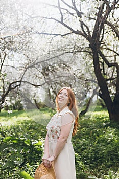 Red-haired girl walks in a spring blooming apple orchard