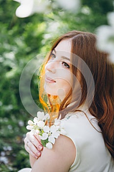 Red-haired girl walks in a spring blooming apple orchard