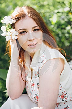 Red-haired girl walks in a spring blooming apple orchard