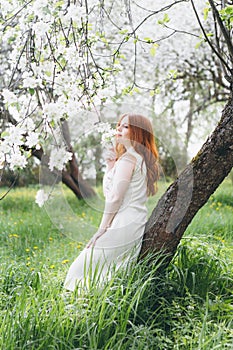 Red-haired girl walks in a spring blooming apple orchard