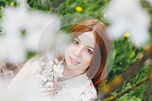 Red-haired girl walks in a spring blooming apple orchard