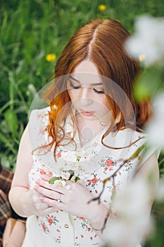 Red-haired girl walks in a spring blooming apple orchard