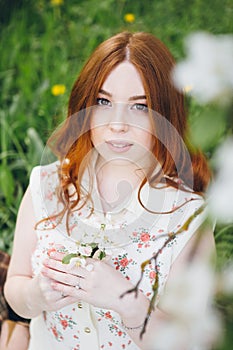 Red-haired girl walks in a spring blooming apple orchard