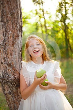 Red-haired girl in a white dress with a green apple in her hands