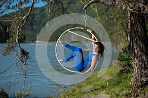 Red-haired gymnast in a blue suit doing the difficult exercises at the air ring in nature