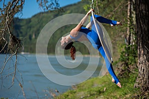 Red-haired gymnast in a blue suit doing the difficult exercises at the air ring in nature