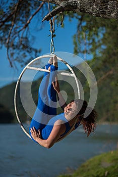 Red-haired gymnast in a blue suit doing the difficult exercises at the air ring in nature