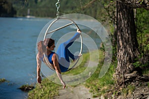 Red-haired gymnast in a blue suit doing the difficult exercises at the air ring in nature