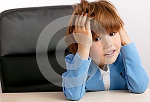 Red-haired kid touching his head while sitting at the table