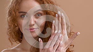 Red-Haired Lady Applying Moisturizer Cream On Hand Over Beige Background