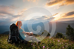 Red-haired lady with backpack in the mountains at sunset