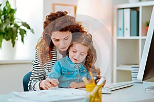 Red-haired mom helping her little girl holding pen and writing