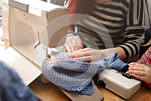Red haired mother spends famnily time together with enthusiastic young girl helping her while sewing at a compact sewing machine