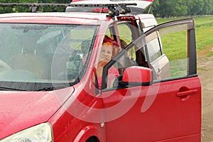 red-haired overweighted elderly woman sits in a red car on the green background.