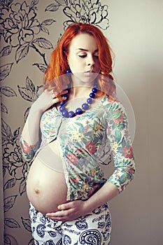 Red-haired pregnant woman with blue beads on her neck in the studio