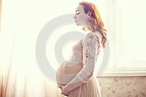 Red-haired pregnant woman in a delicate pink lace dress